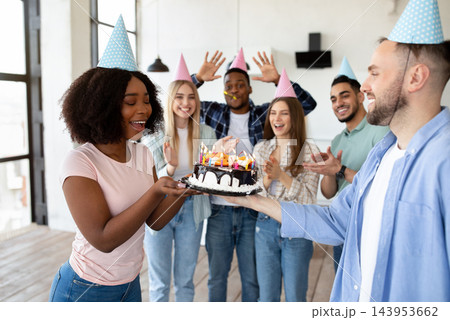 Group of cool multiethnic millennials celebrating birthday, presenting tasty cake to their black female b-day friend at home. Diverse youth wearing party hats, having fun holiday Group of cool multiethnic millennials celebrating birthday, presenting tasty cake to their black female b-day friend at home. Diverse youth wearing party hats, having fun holiday 143953662