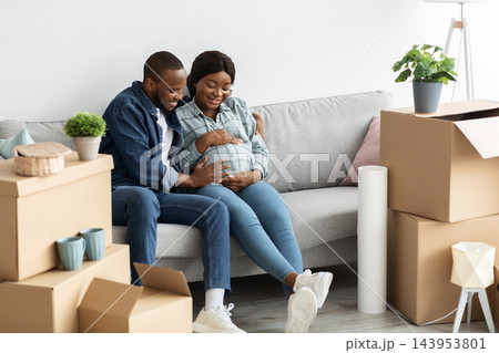 Happy Young Black Spouses Moving To New Apartment, African American Husband And Pregnant Wife Sitting On Couch Among Unpacked Cardboard Boxes After Relocation, Family Housing And Real Estate Concept Happy Young Black Spouses Moving To New Apartment, African American Husband And Pregnant Wife Sitting On Couch Among Unpacked Cardboard Boxes After Relocation, Family Housing And Real Estate Concept 143953801