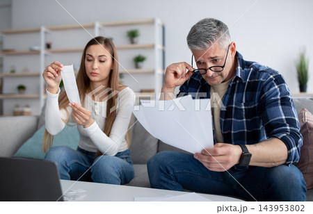 Family budget planning concept. Married mature couple with documents and bills counting their finances on laptop at home. Senior spouses budgeting household expenses, managing money online 143953802