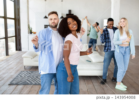 Multiracial young couple partying with their diverse friends, dancing and drinking beer at home. Cheerful millennials socializing, moving to music, enoying fun weekend in living room Multiracial young couple partying with their diverse friends, dancing and drinking beer at home. Cheerful millennials socializing, moving to music, enoying fun weekend in living room 143954008