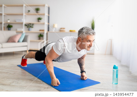 Sport during quarantine. Mature man doing push-up exercises on fists, training in living room at home, free space. Sport exercises, active lifestyle during quarantine 143954477