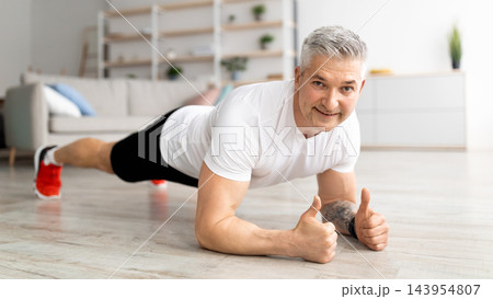 Domestic workout. Sporty mature man standing in elbow plank and strengthening abs muscles, doing fitness training in living room at home, leading healthy active lifestyle, panorama Domestic workout. Sporty mature man standing in elbow plank and strengthening abs muscles, doing fitness training in living room at home, leading healthy active lifestyle, panorama 143954807