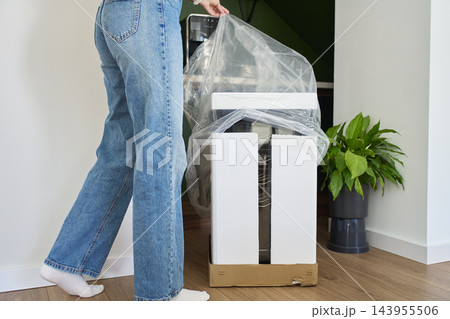 Woman removes protective plastic and foam packaging from new wine cooler 143955506