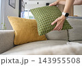 Woman arranging decorative throw pillows on sofa. Hands placing cushion next to yellow pillow 143955508