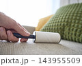 Hand using lint roller to clean fabric sofa upholstery 143955509