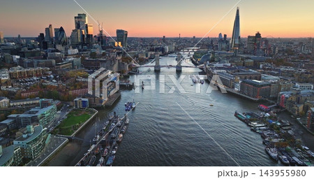 Travel and explore London. River Thames and the iconic Tower Bridge spanning the cityscape with various boats navigating the waterway. Aerial drone flight over modern England capital city skyline 143955980