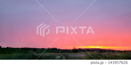 Panoramic meadow and distant treeline beneath vibrant magenta and orange sunset sky with glowing horizon light, peaceful twilight landscape scene, wide horizontal view Panoramic meadow and distant treeline beneath vibrant magenta and orange sunset sky with glowing horizon light, peaceful twilight landscape scene, wide horizontal view 143957626