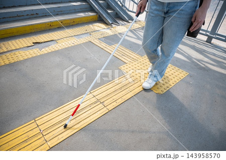 A blind woman walks using a cane and tactile tiles. 143958570