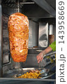 Chicken Doner Kebab. Chicken doner kebab meat stacked on vertical rotisserie inside commercial street food kitchen with golden French fries beside stainless steel equipment 143958669