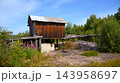 Abandoned wooden building elevated on stilts in a rural landscape, Karelia, Russia. Dilapidated shed with a wooden walkway surrounded by overgrown vegetation and fireweed under a blue sky 143958697