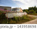 Abandoned rusty white boat resting on land by the White Sea, Karelia. Overgrown rural landscape with tall grass and pink flowers. Nature reclaiming old broken machinery and decaying metal 143958698