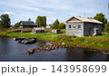Rural village with old weathered wooden houses on a river bank, Karelia, Russia. Small boats moored by the rocky shore on a sunny summer day. Traditional countryside landscape and rustic scene 143958699