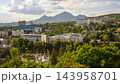 Elevated panoramic view of a green resort town with a prominent mountain peak in the background. Cityscape featuring a park, trees, and mixed architecture in Pyatigorsk. Summer travel destination 143958701