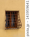 Rusty wrought iron grate on small window in yellow plastered wall 143959641