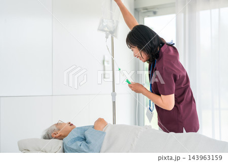 点滴を確認する女性看護師とベッドで休む高齢者 143963159