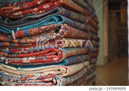 A neatly arranged stack of folded, patterned rugs displayed inside a shop interior A neatly arranged stack of folded, patterned rugs displayed inside a shop interior 143964669