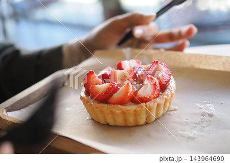 Person uses a phone beside a strawberry tart at a cafe 143964690