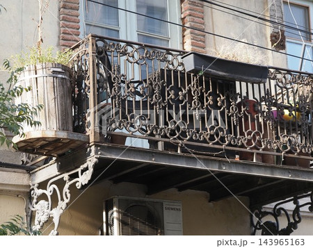 Vintage balcony with ornate black wrought iron railing on a light brick building facade. 143965163