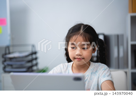 Young girl using tablet computer at home focused on screen digital learning technology indoors child education concept Young girl using tablet computer at home focused on screen digital learning technology indoors child education concept 143970040