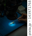 A technician repairs a smartphone and looks at a microchip through a microscope. 143971768