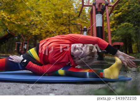 Mature woman practicing yoga and stretching outdoors in an autumn park. Active senior enjoying healthy aging, fitness, and vitality through outdoor workout and mindfulness. 143972210