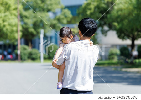 公園で小さな娘を抱っこする父親の後ろ姿 143976378
