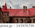 Red roofed brick manor house with a pointed tower beneath dramatic overcast skies and heavy clouds 143976796