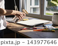 Person sprays water onto textured canvas surrounded by painting supplies 143977646