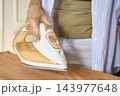 Close up of woman ironing brown fabric with electric steam iron on ironing board 143977648