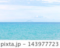 Minimalist turquoise seascape with pale sky, calm horizon, and distant island in a wide panorama 143977723