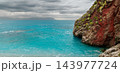 Turquoise coastal bay meets a rugged red rock headland beneath a dramatic cloudy sky 143977724
