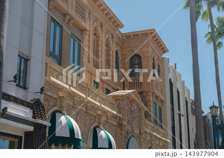 An ornate classical building features arched windows, balconies, decorative stonework, and striped awnings. Tall palm trees rise beside the elegant facade under a clear blue sky. An ornate classical building features arched windows, balconies, decorative stonework, and striped awnings. Tall palm trees rise beside the elegant facade under a clear blue sky. 143977904