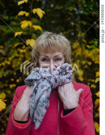 Happy senior woman in pink coat smiling outdoors in autumn park. Active elderly lifestyle, healthy aging and seasonal wellness concepts. 143980608