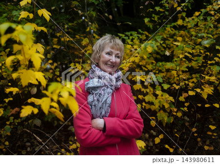 Happy senior woman in pink coat smiling outdoors in autumn park. Active elderly lifestyle, healthy aging and seasonal wellness concepts. 143980611