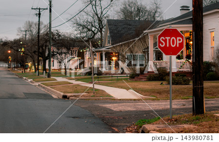 JEFFERSON, TEXAS: A red stop sign stands at a quiet street corner in a historic residential neighborhood illuminated with Christmas lights at dusk. 143980781