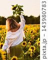 Woman enjoying a quiet moment in a blooming sunflower field while lifting a flower toward the warm evening sunlight. The serene outdoor scene reflects tranquility, mindfulness and rural summer 143980783