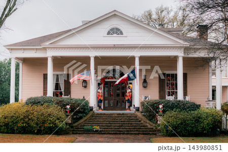 JEFFERSON, TEXAS: A grand beige Southern plantation-style historic home with white columns, grand brick steps, nutcrackers, an American flag, and a Texas flag. 143980851