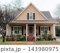 JEFFERSON, TEXAS: A cozy beige craftsman house with a red front door, white rocking chairs on the front porch, brick foundation, and holiday decorations. 143980975