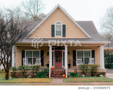 JEFFERSON, TEXAS: A cozy beige craftsman house with a red front door, white rocking chairs on the front porch, brick foundation, and holiday decorations. JEFFERSON, TEXAS: A cozy beige craftsman house with a red front door, white rocking chairs on the front porch, brick foundation, and holiday decorations. 143980975