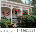 JEFFERSON, TEXAS: A white historic home's front porch decorated for the holidays with large red hanging ornament balls, string lights, and festive holiday decor. 143981114