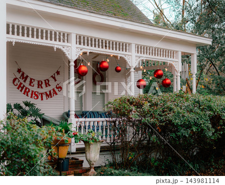 JEFFERSON, TEXAS: A white historic home's front porch decorated for the holidays with large red hanging ornament balls, string lights, and festive holiday decor. JEFFERSON, TEXAS: A white historic home's front porch decorated for the holidays with large red hanging ornament balls, string lights, and festive holiday decor. 143981114