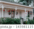 JEFFERSON, TEXAS: A white historic home's front porch decorated for the holidays with large red hanging ornament balls, string lights, and festive holiday decor. 143981115