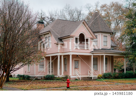 JEFFERSON, TEXAS: A stunning two-story pink Victorian home featuring a corner turret tower, wraparound front porch, and historic architectural details surrounded by fall foliage. 143981180