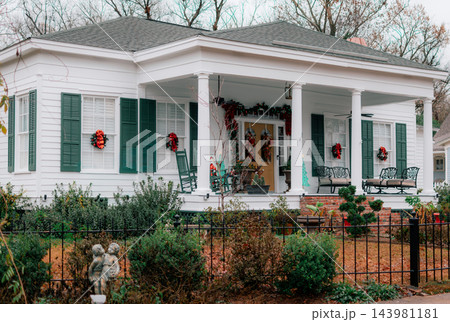 JEFFERSON, TEXAS: A classic white historic home adorned for Christmas with green shutters, red bows, wreaths, a wrought-iron fence, and holiday decorations on the front porch. 143981181