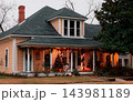 JEFFERSON, TEXAS: A warm light-orange historic house decorated for Christmas at dusk, featuring illuminated string lights, festive garland, and Christmas trees on the porch. 143981189