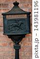 JEFFERSON, TEXAS: An ornate antique black cast-iron mailbox mounted on a pedestal in front of a red brick wall featuring a embossed horseback mail rider design. 143981196