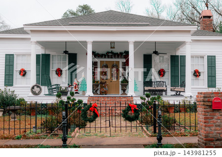 JEFFERSON, TEXAS: A classic white historic home adorned for Christmas with green shutters, red bows, wreaths, a wrought-iron fence, and holiday decorations on the front porch. 143981255