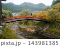 UDA, NARA, JAPAN: A traditional red vermilion arched wooden bridge spanning across a shallow rocky river toward Murou-ji temple amidst autumn trees and misty forested mountains. 143981385