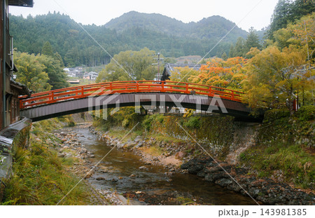 UDA, NARA, JAPAN: A traditional red vermilion arched wooden bridge spanning across a shallow rocky river toward Murou-ji temple amidst autumn trees and misty forested mountains. 143981385