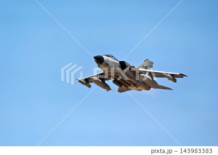 Military combat aircraft flying against a clear blue sky, showing drop tanks and extended wings during flight Military combat aircraft flying against a clear blue sky, showing drop tanks and extended wings during flight 143983383